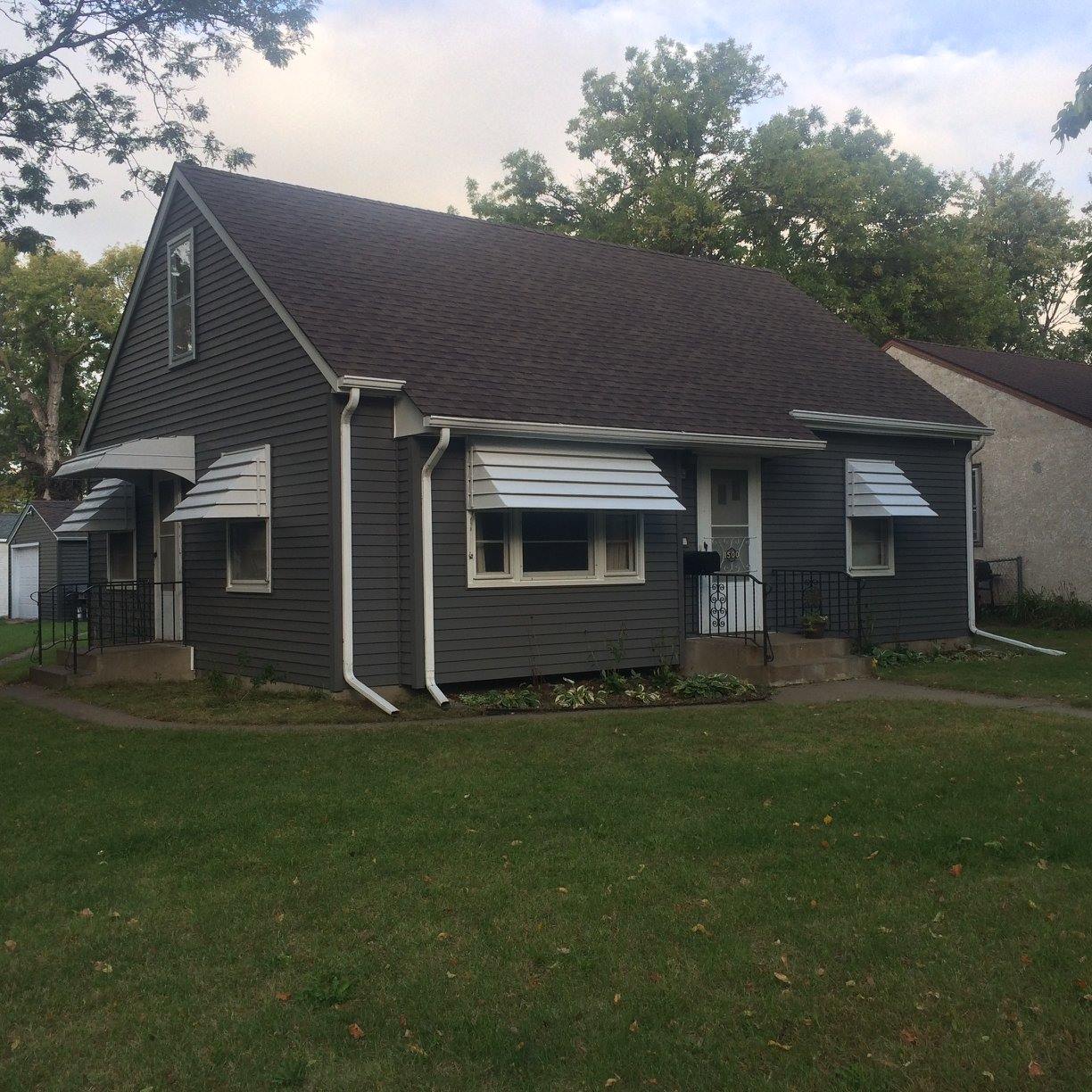 Cape cod home in Blaine, MN with new dark gray lap siding, white window awnings, and white trim by Right Away Construction