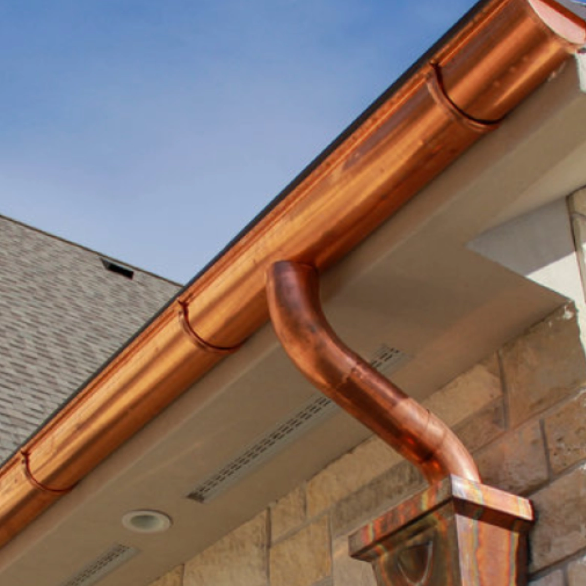 Copper half-round gutter and downspout installed along a residential roofline