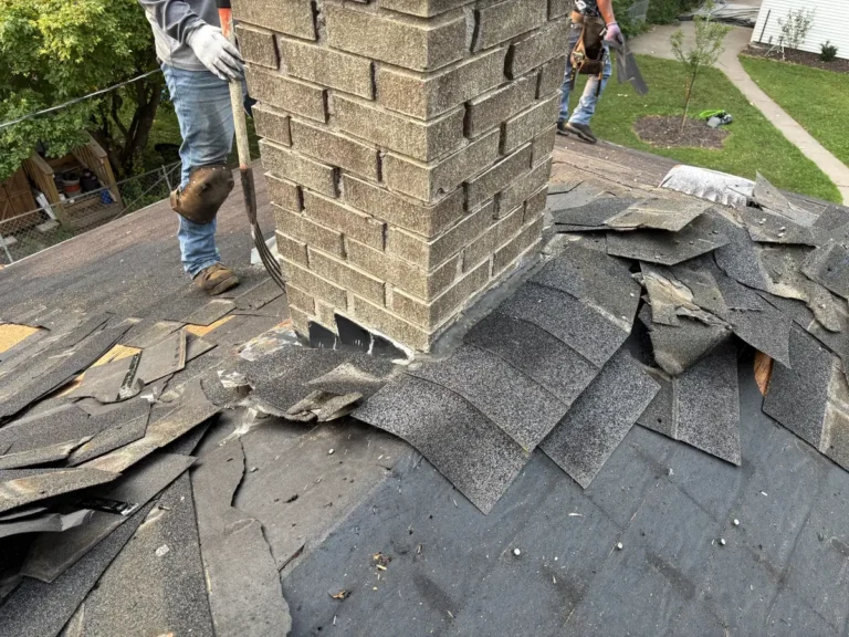 Crew member working beside a brick chimney during a roof tear-off in Minneapolis.
