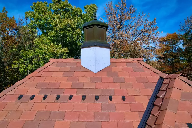 Chimney centered on an upper DaVinci synthetic slate roof plane, with snow guards and flashing visible.