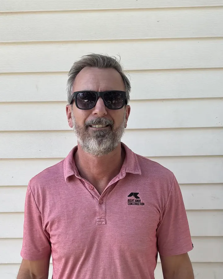 Josh Kujawa, president and owner of Right Away Construction, in a company polo in front of white siding.