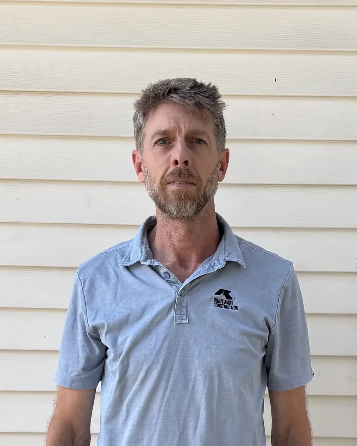 Lewis May, manager and master roofer at Right Away Construction, in a company polo in front of white siding.