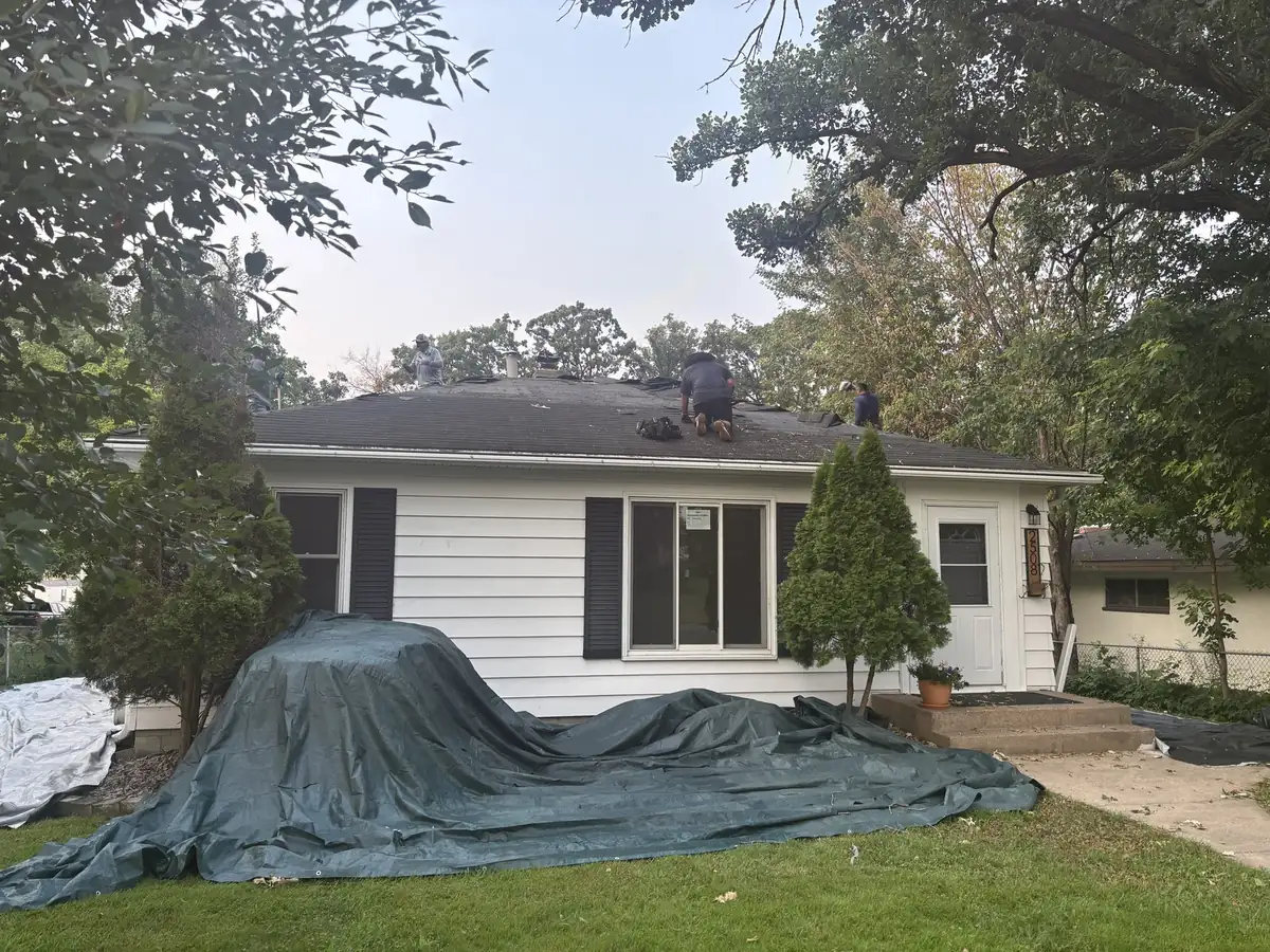 Roof tear-off underway on a Minneapolis home with tarps protecting the landscaping below.
