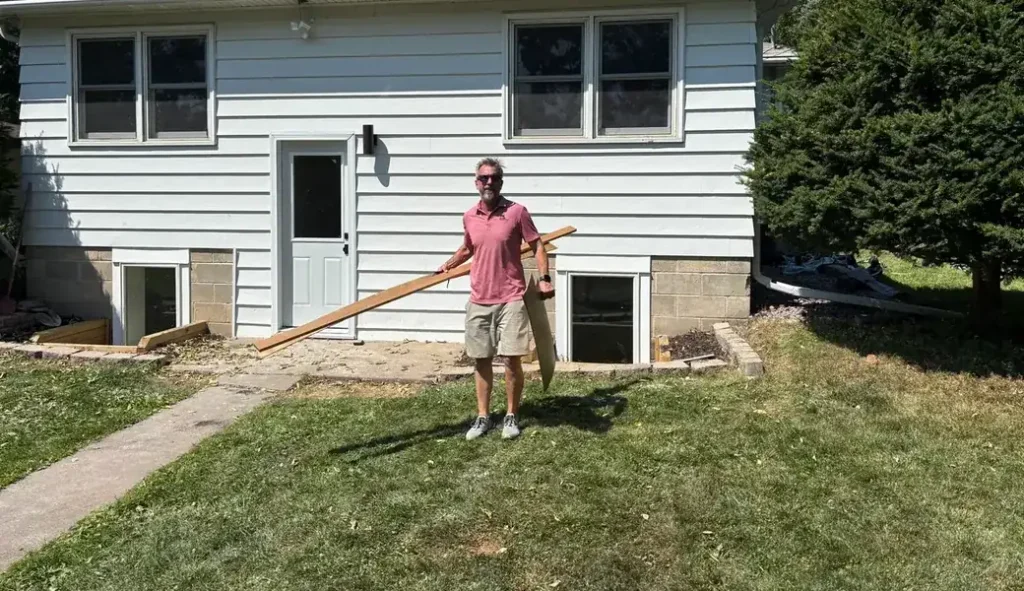 Josh Kujawa of Right Away Construction on a job site behind a Minneapolis home, carrying lumber across the yard.