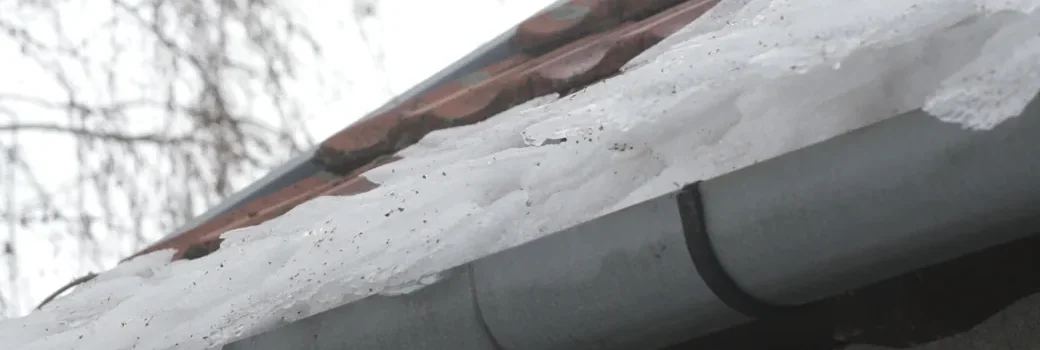 Ice built up along a roof eave and over the gutter in winter