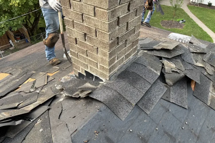 Crew member working beside a brick chimney during a roof tear-off in Minneapolis.