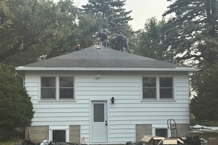 Rear elevation of a Minneapolis home with crew on the roof and materials staged below.