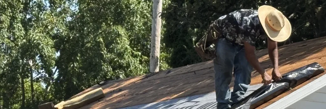 Roofer in a straw hat rolling out synthetic underlayment during a roof replacement